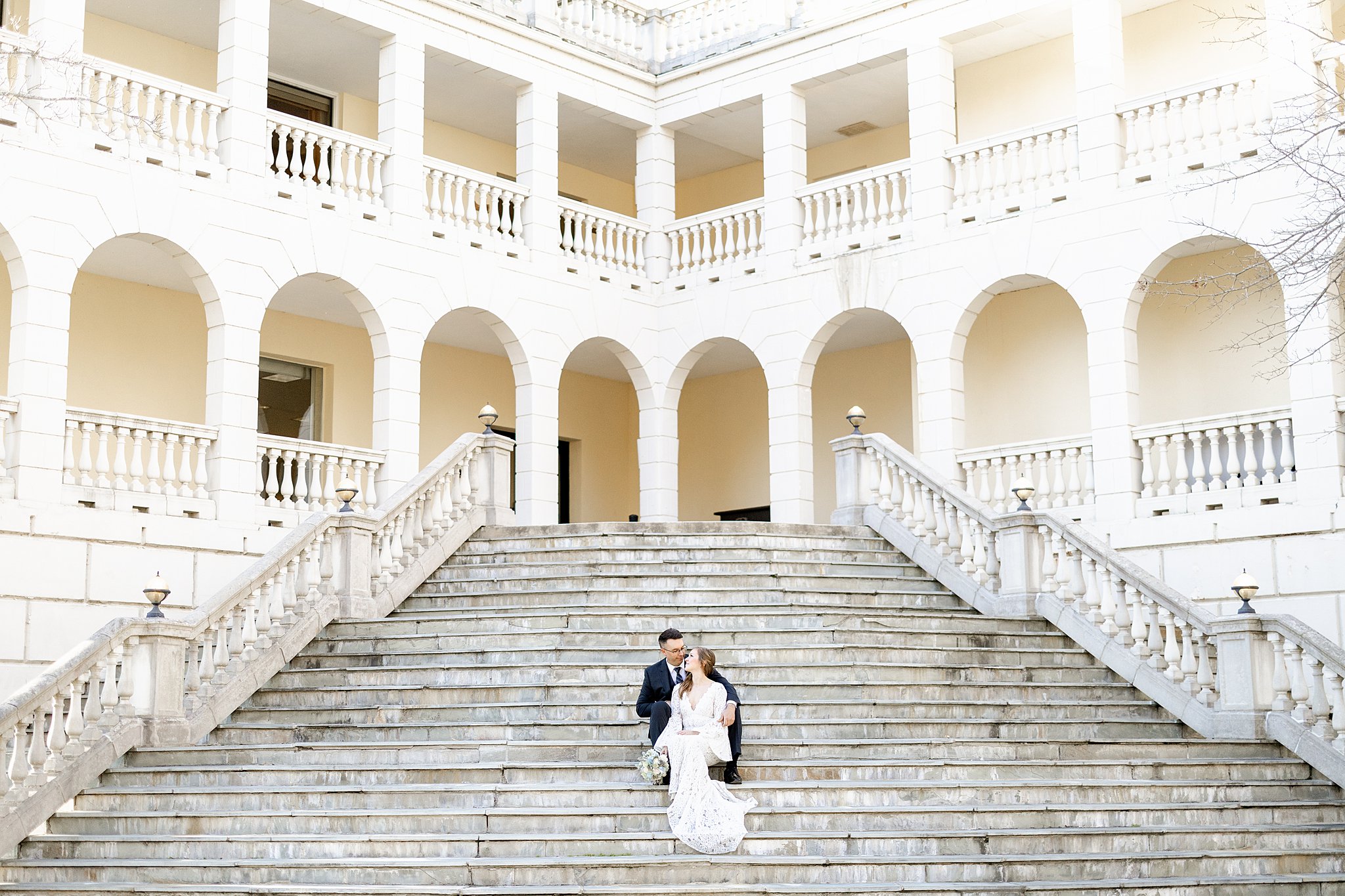 Newlyweds sit on a grand staircase of a large ornate archway building virginia elopement