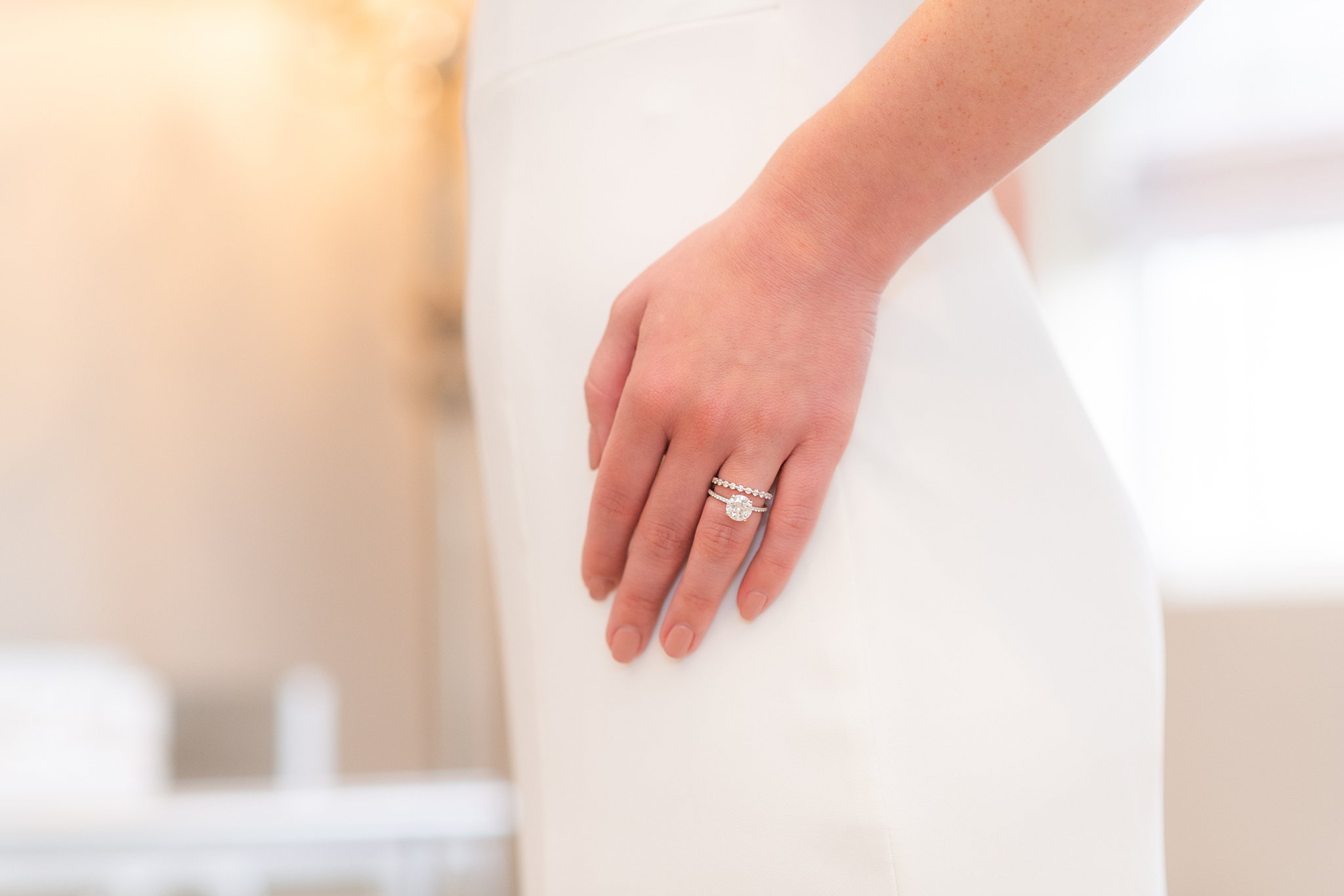 A bride in a white silk dress wears her wedding band and engagement ring on one hand