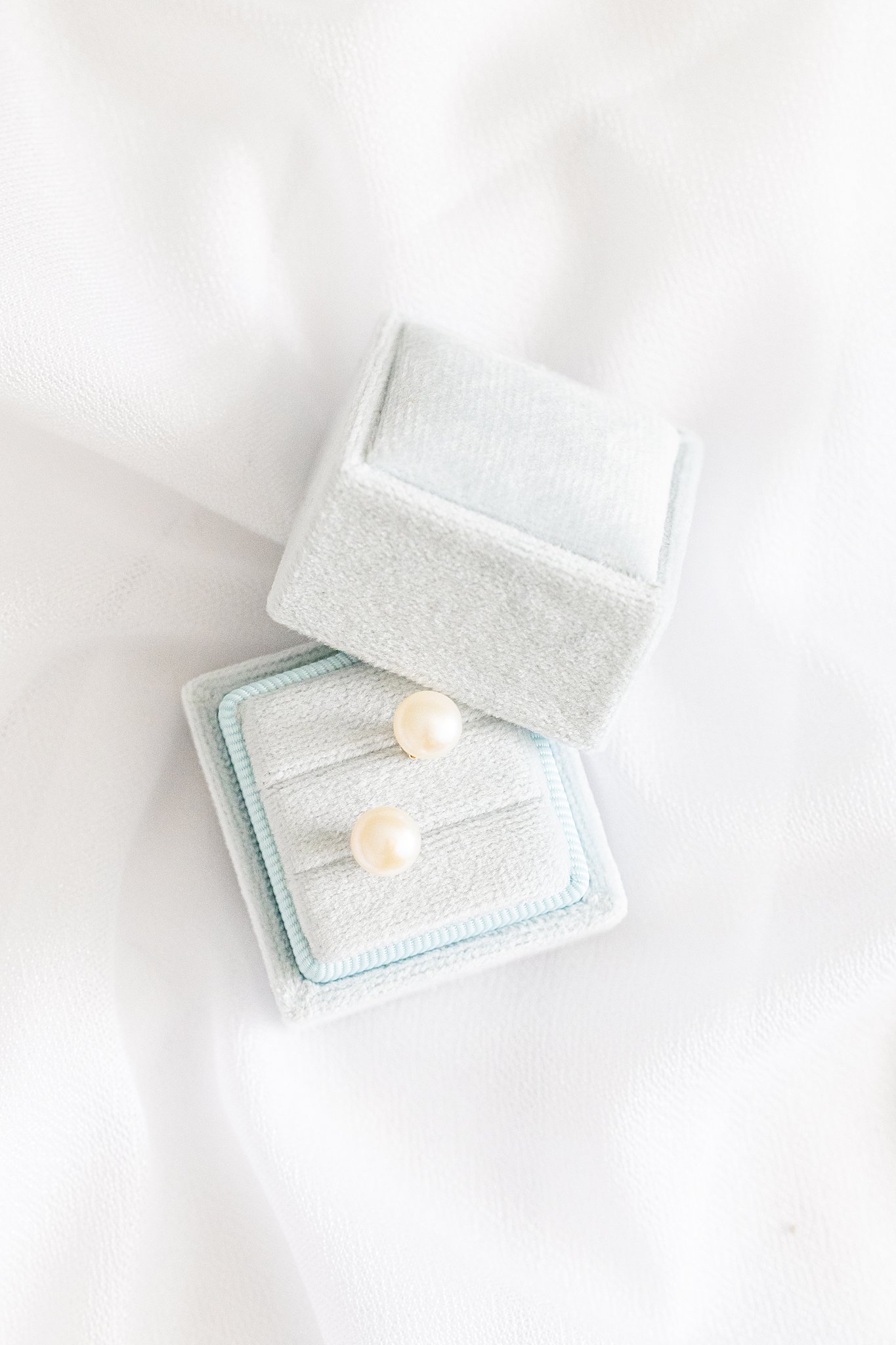A pair of pearl earrings sit in their jewelry box on a white fabric virginia wedding planner