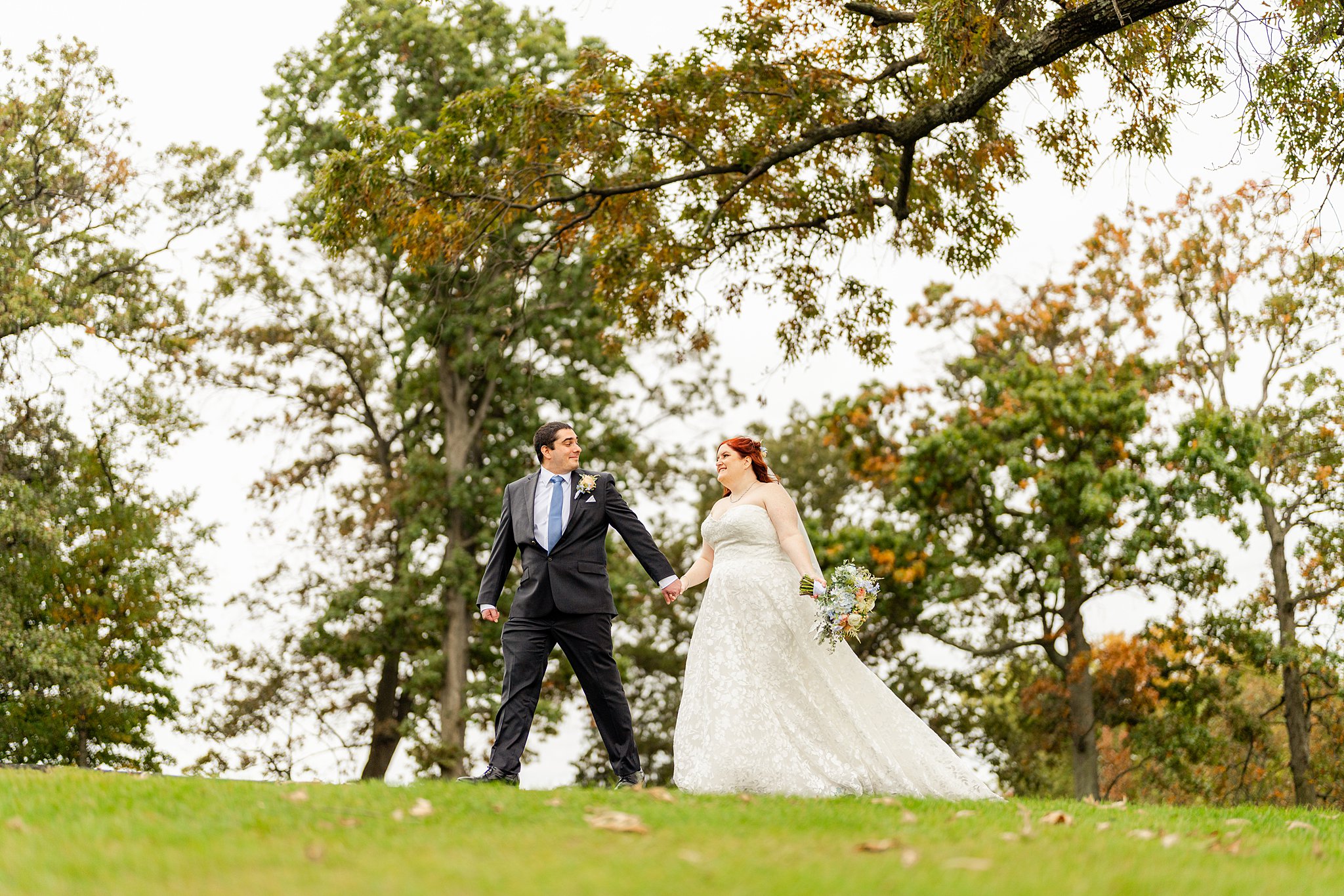 Newlyweds hold hands while walking through a park with tall trees wedding venues in northern virginia